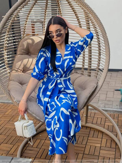 Woman in a blue patterned dress sitting in a wicker chair outdoors.