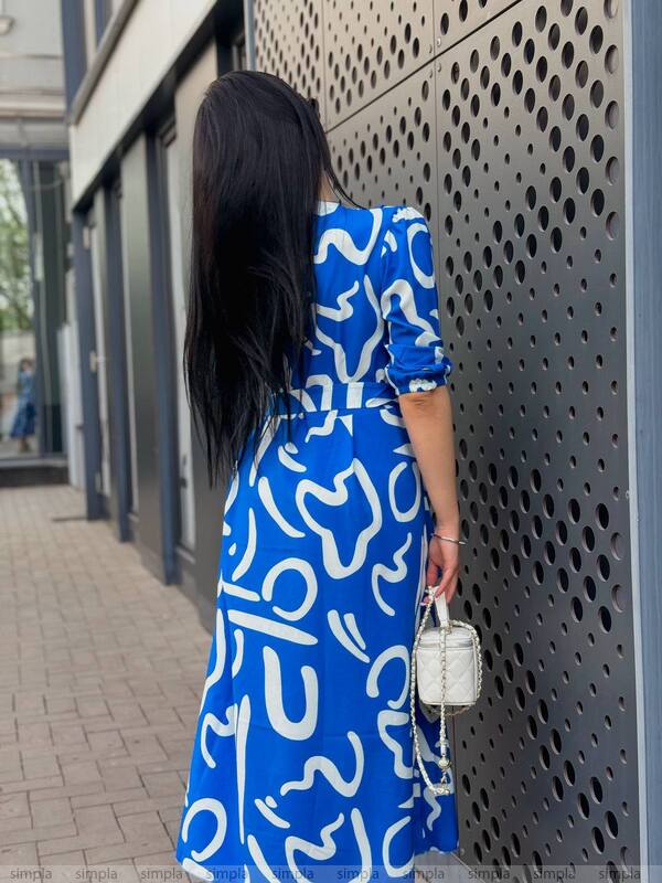 Woman in a blue patterned dress standing against a textured wall.