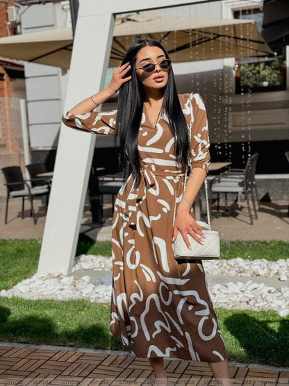 Woman in a brown and white patterned dress standing outdoors.
