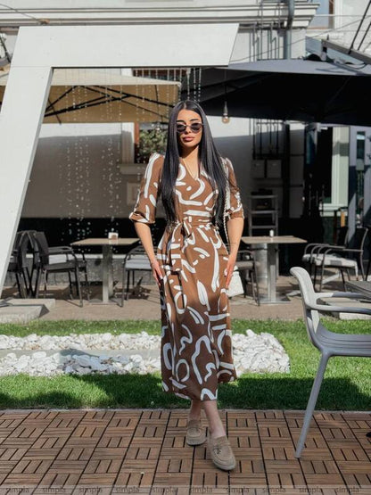 Woman in a patterned dress standing outdoors with tables and chairs in the background