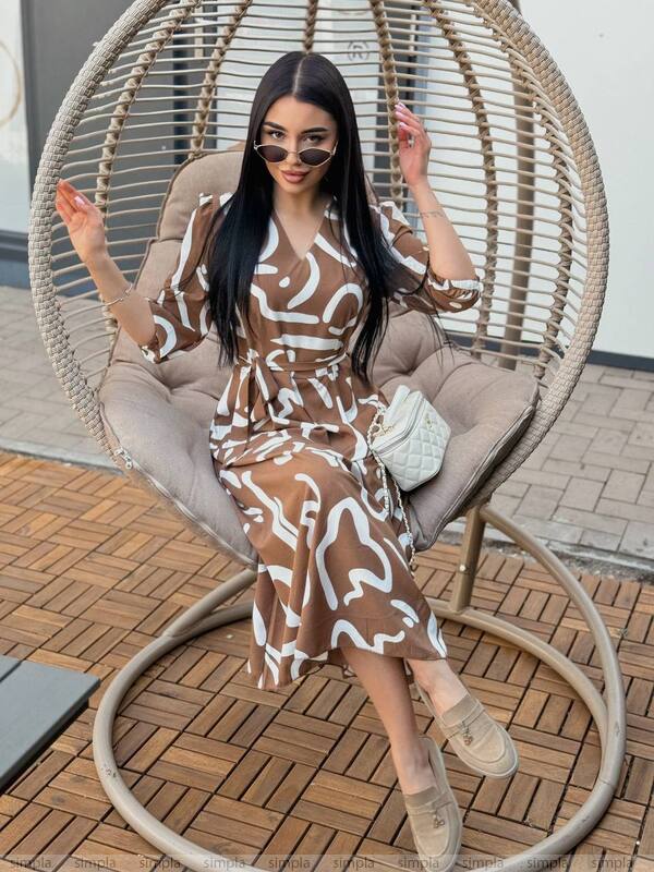 Woman in a patterned dress sitting on a wicker chair outdoors.