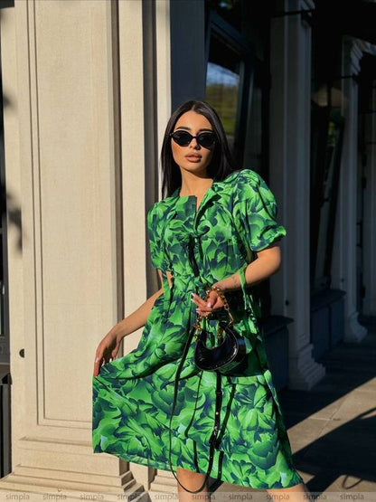 Woman wearing a green dress with leaf pattern standing outdoors.