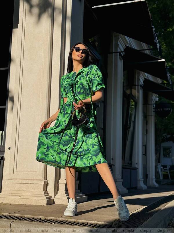 Woman in a green floral dress standing outdoors near a building entrance.