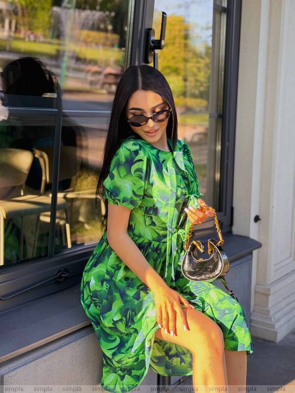 Woman in a green dress holding a handbag, sitting on a bench outside.