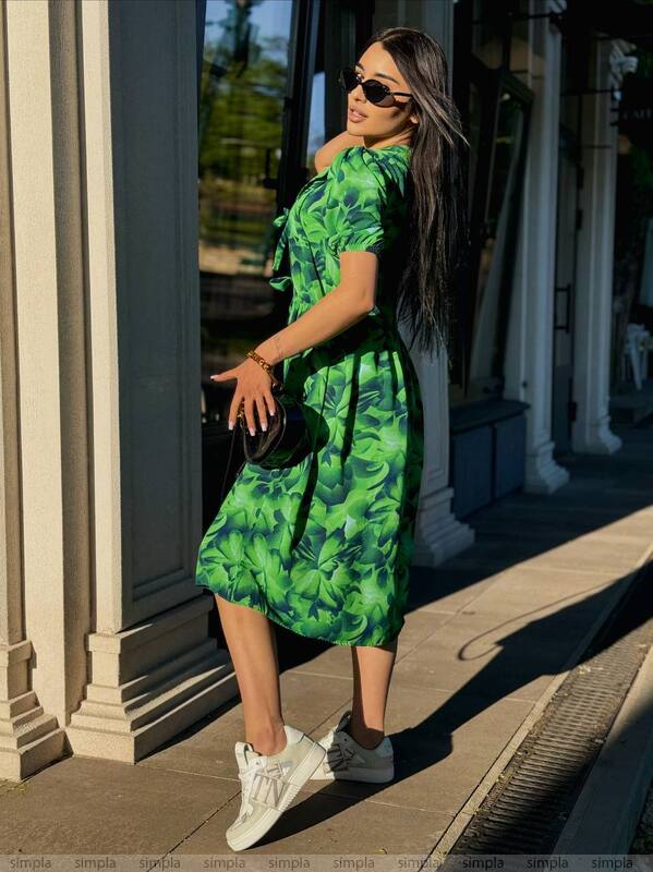 Woman in a green floral dress standing on a sidewalk