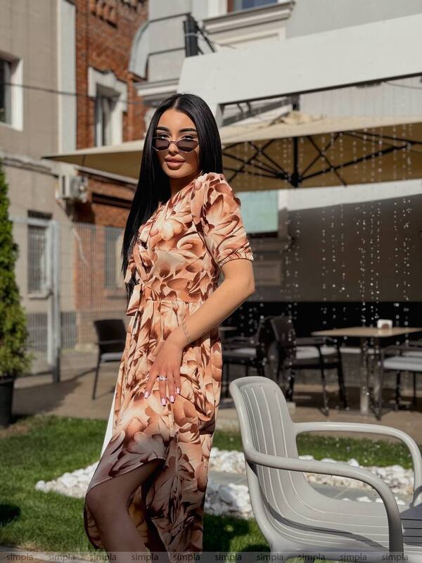 Woman in a floral dress standing outdoors with chairs and tables in the background