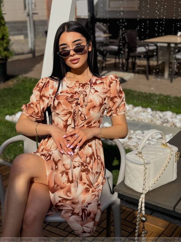 Woman in a floral dress sitting outdoors with a handbag next to her.