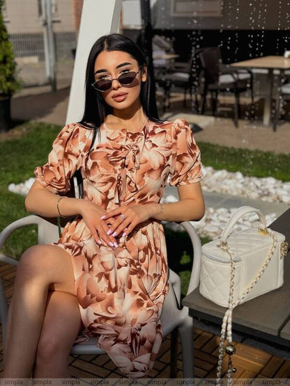 Woman in a floral dress sitting outdoors with a handbag next to her.