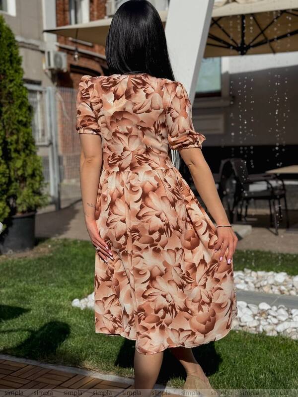 Woman wearing a floral dress standing outdoors on a grassy area.