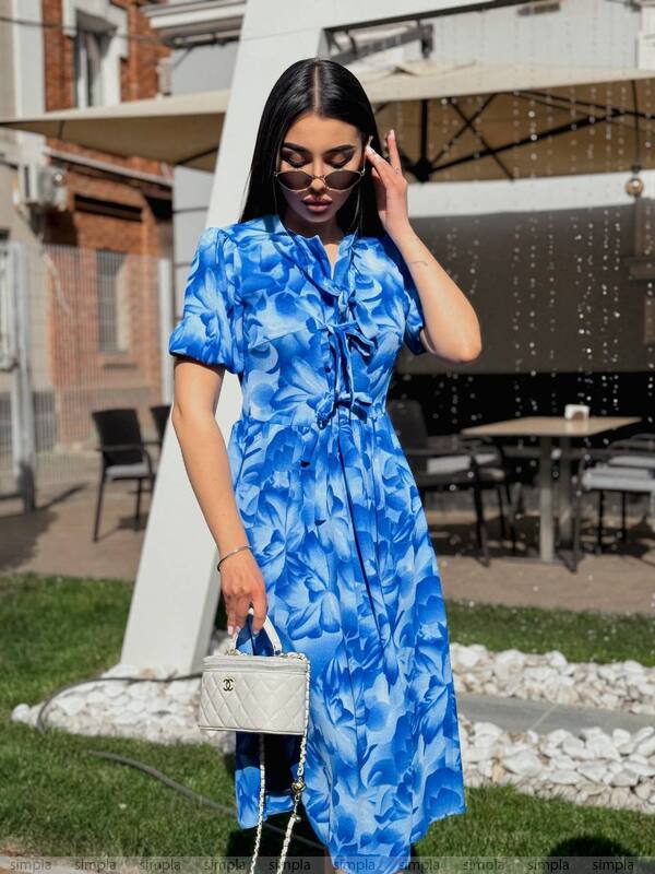 Woman in a blue floral dress standing outdoors with a blurred background