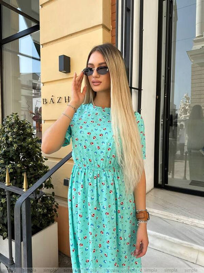 Woman in a turquoise floral dress standing outside a building with 'Bázh' sign.