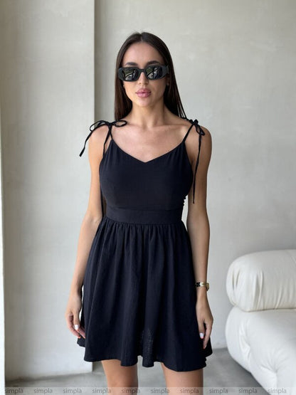 Woman wearing a black dress with thin straps in a minimal indoor setting