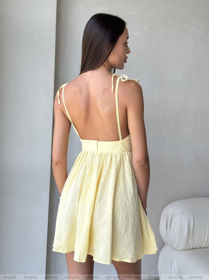 Woman wearing a light yellow dress with thin straps against a plain background