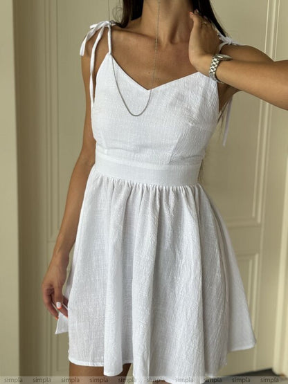 White dress with thin straps being adjusted against a neutral background