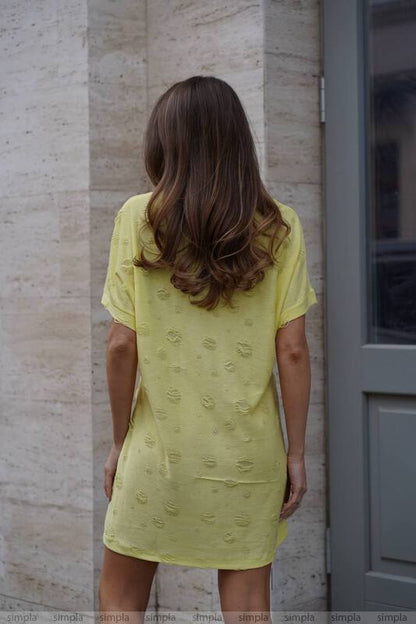 Woman wearing a yellow dress standing against a textured wall.