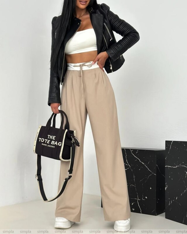 Person wearing a black jacket, white top, beige pants, and holding a black tote bag with a white background.