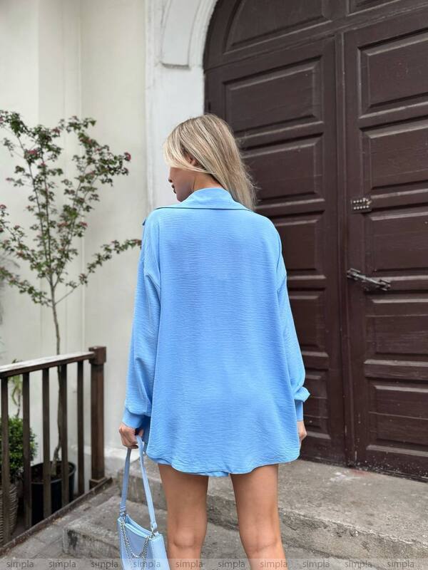 Person wearing a light blue oversized shirt in front of a brown door.