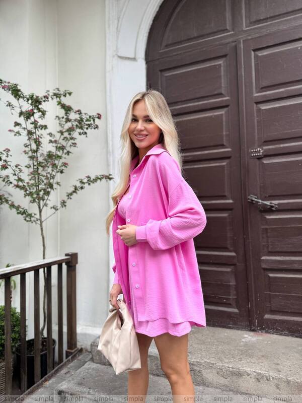 Woman wearing a pink shirt dress standing in front of a large door.
