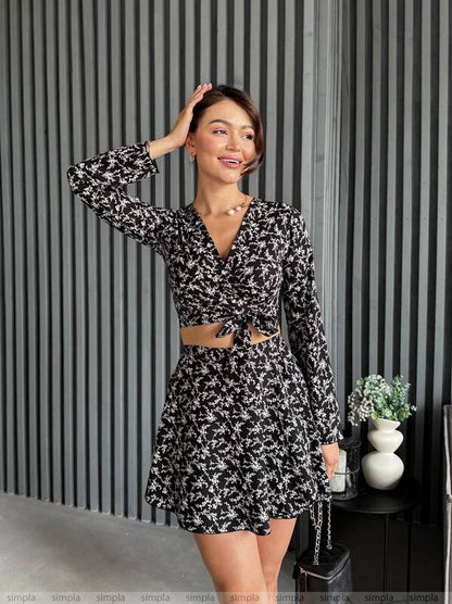 Woman wearing a black and white patterned dress against a striped wall.