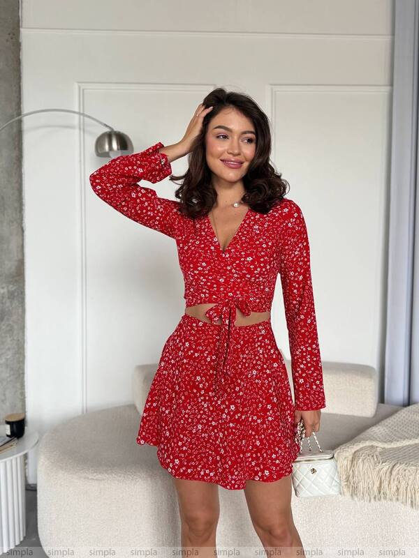 Woman wearing a red floral dress in a room with a white couch and light-colored walls.