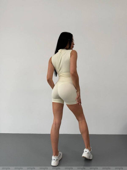 Person wearing a beige sleeveless top and shorts set against a plain background
