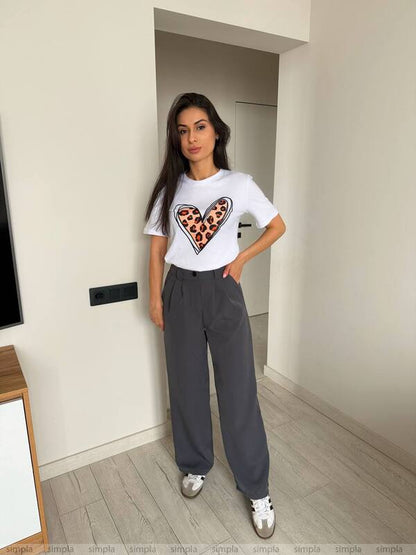 Woman wearing a white t-shirt with a heart design and gray pants in a room.