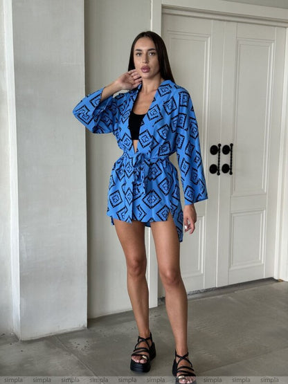 Woman wearing a blue patterned outfit standing in a room with a white door.