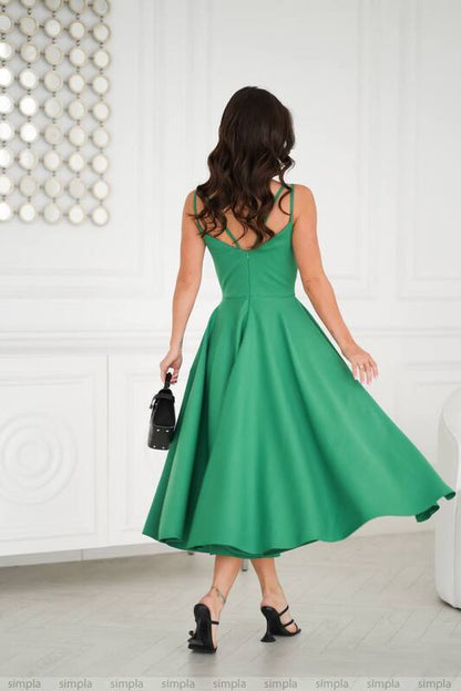 Woman wearing a green dress holding a black handbag in a minimalistic setting