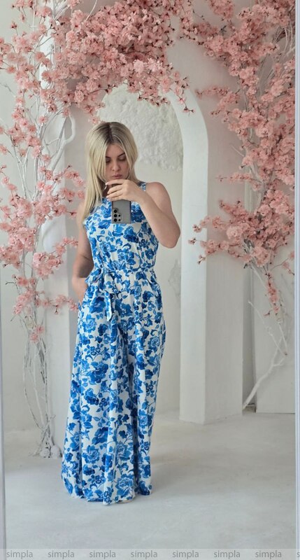 Woman in a blue floral dress standing in front of pink floral decorations.