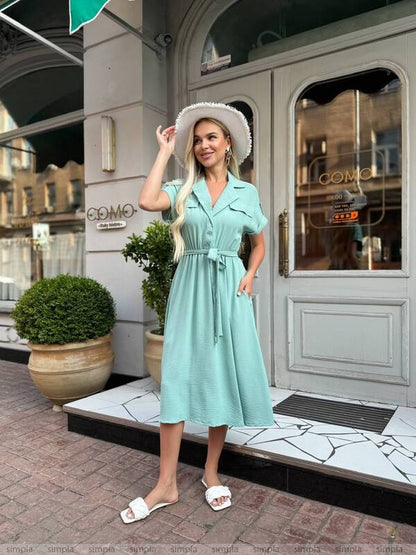 Woman in a light blue dress standing outside a store with a white hat.