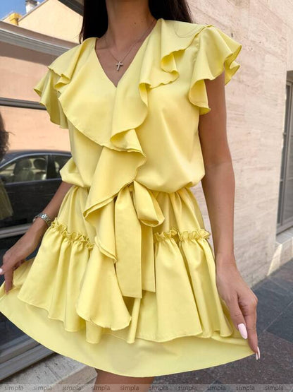 Woman wearing a yellow ruffled dress against a building background