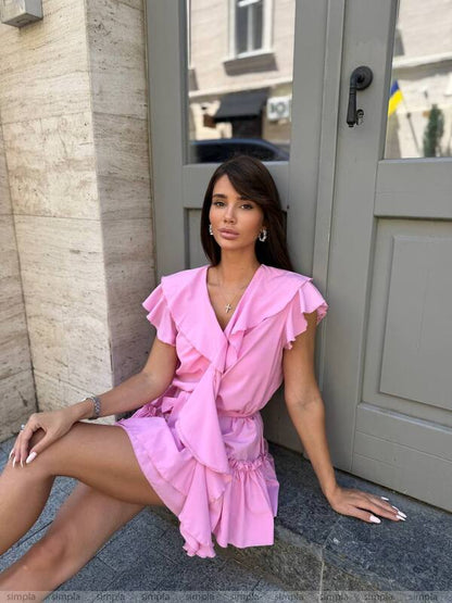 Woman in a pink dress sitting on a step outside a building.