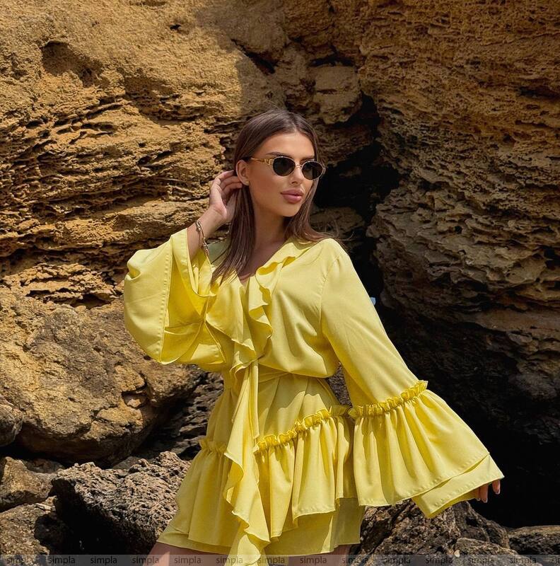 Woman in a yellow dress standing against a rocky background