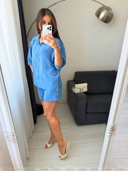 Woman taking a mirror selfie wearing a blue outfit in a room with a gray sofa.