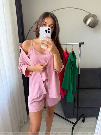 Person wearing a pink outfit taking a mirror selfie in a room with a coat rack and gray sofa.