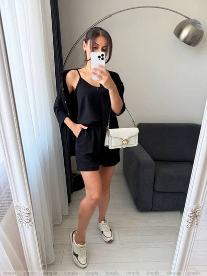 Person taking a mirror selfie wearing a black outfit with a white bag in a room.
