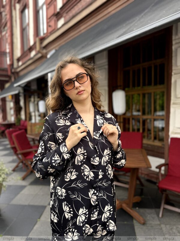 Woman wearing a black floral kimono in an outdoor setting with red chairs and a building in the background.