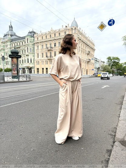 Woman in a beige outfit standing on a city street with classical architecture in the background