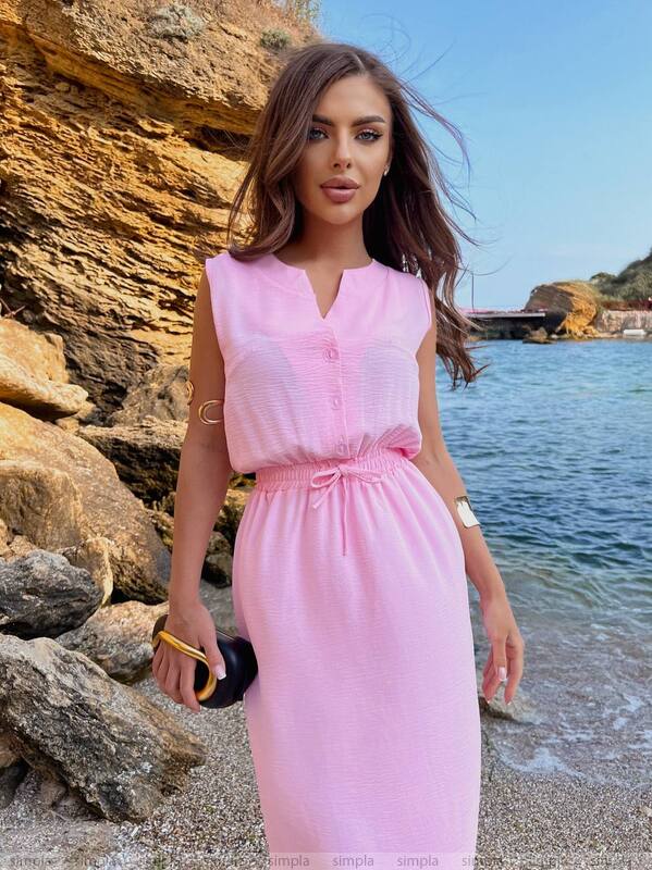 Woman in a pink dress standing by a rocky coastline with water in the background