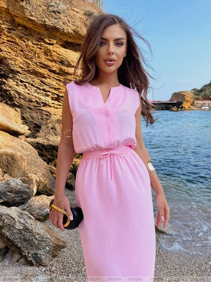 Woman in a pink dress standing by a rocky coastline with water in the background