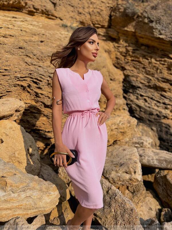 Woman in a pink dress standing against a rocky background