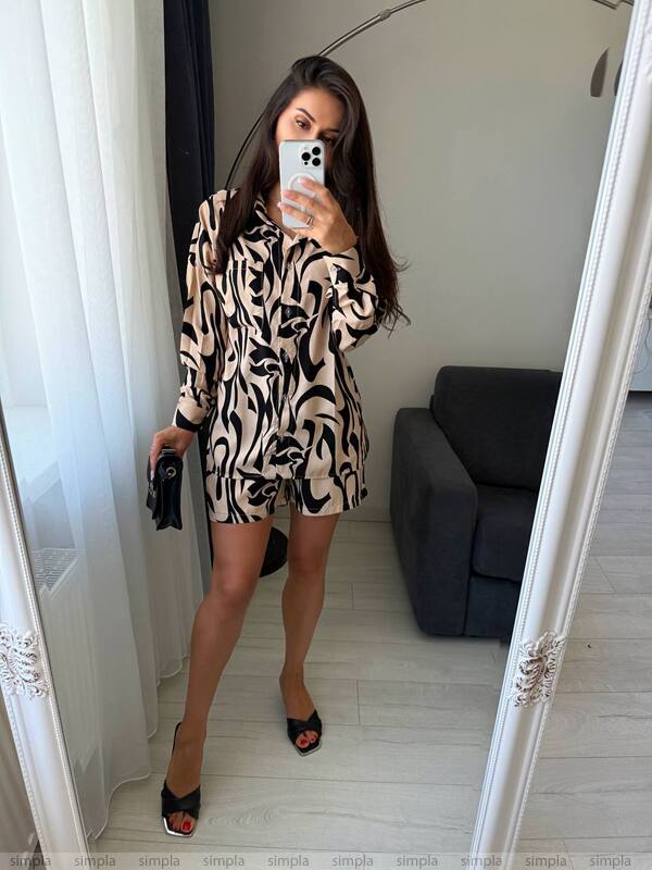 Woman taking a mirror selfie wearing a patterned outfit in a room with a gray sofa.