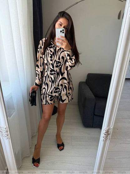 Woman taking a mirror selfie wearing a patterned outfit in a room with a gray sofa.