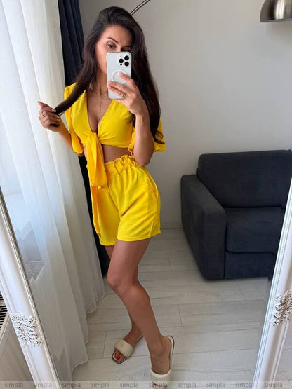 Woman in a yellow outfit taking a mirror selfie in a room with a gray sofa.