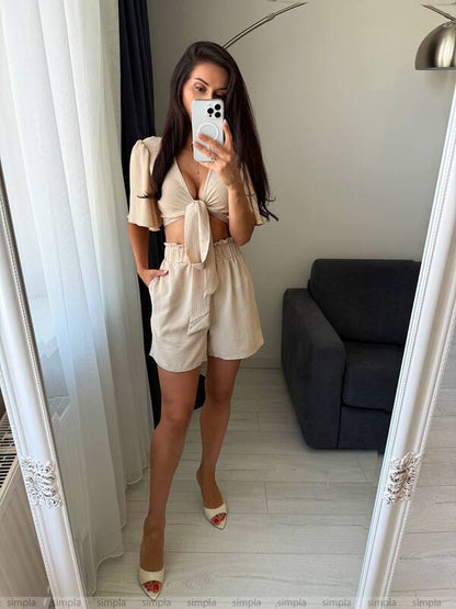 Woman taking a mirror selfie wearing a beige outfit in a room with a gray sofa.