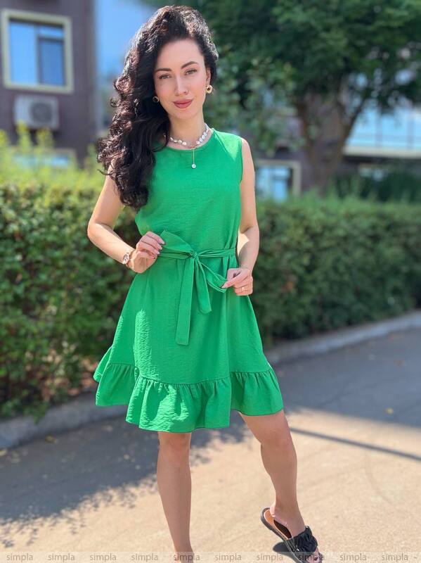 Woman wearing a green dress standing outdoors with greenery in the background