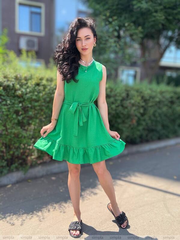 Woman in a green dress standing outdoors with greenery in the background