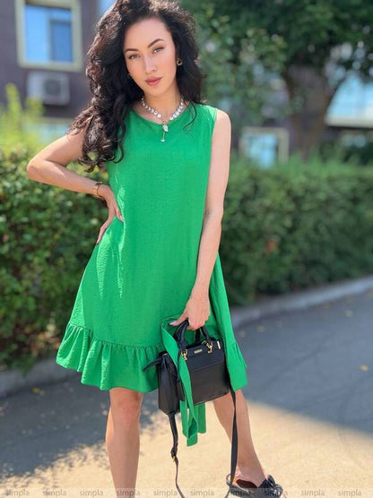 Woman in a green dress holding a black handbag outdoors.