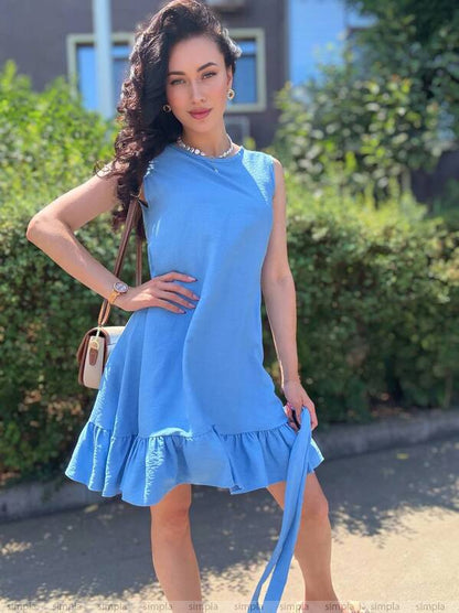 Woman in a blue dress standing outdoors with greenery in the background