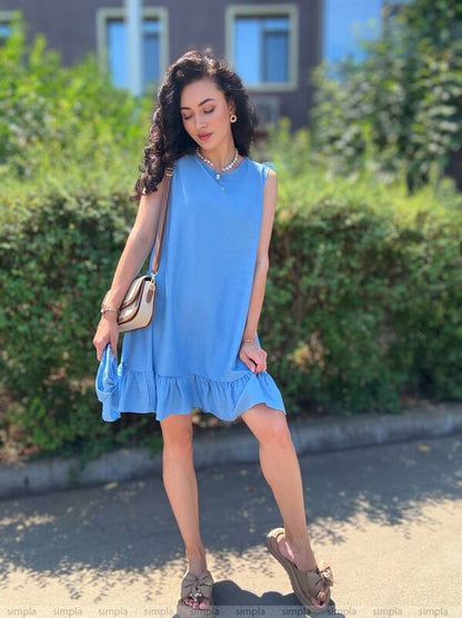 Woman wearing a blue dress standing outdoors with greenery in the background